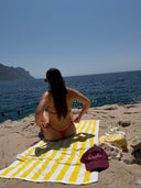 Honëlo Beach Day Cap in Merlot resting on a striped beach towel by the ocean