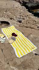 Honëlo Beach Break Towel in Lemon Stripe, flat lay on rocks with shells and sunglasses