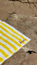Honëlo Beach Break Towel folded on rocks, embroidered logo detail